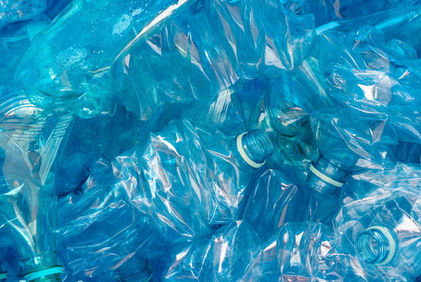 Verpletterde plastic flessen op blauwe achtergrond. Een symbool van milieuvervuiling en recyclinguitdagingen en -successen - Foto, afbeelding