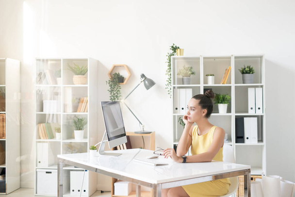 Молода зайнята бізнес-леді в елегантній жовтій сукні, дивлячись на екран комп'ютера під час організації роботи або короткої перерви
 - Фото, зображення