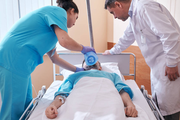 Enfermeira usando máscara de válvula de saco ao fornecer ventilação ao paciente em estado crítico sob controle médico
 - Foto, Imagem