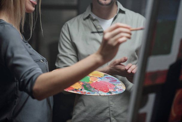 Jovem estudante do estúdio de arte com paleta de cores e seu professor trabalhando juntos sobre nova pintura no cavalete
 - Foto, Imagem