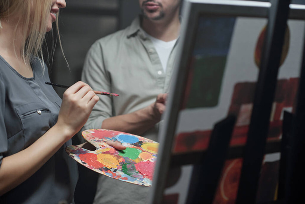 Professeur de peinture consultant son élève avec pinceau et palette de couleurs à la leçon tout en étant debout près du chevalet
 - Photo, image
