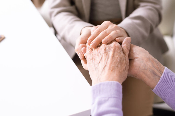 Handen van een jonge vrouw die de gepensioneerde vrouw vasthoudt en tegelijkertijd haar moeder of grootmoeder steunt en troost biedt - Foto, afbeelding