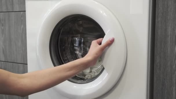 Evlilik yüzüklü bir kadın çamaşır makinesine beyaz giysiler koydu. Çamaşır makinesi yükleniyor. Giysileri çamaşır makinesine yükleyin. Çamaşır makinesini yükle. Çamaşır yıkıyorum. - Video, Çekim