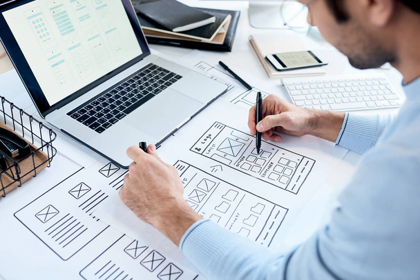 Close-up of busy designer sitting at table with laptop and drawing icons placement for ui design - Photo, Image