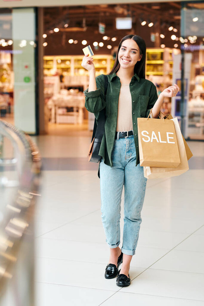 Portrait of cheerful excited young woman in casual outfit using credit card and getting rewarded for making purchases in mall - Fotografie, Obrázek