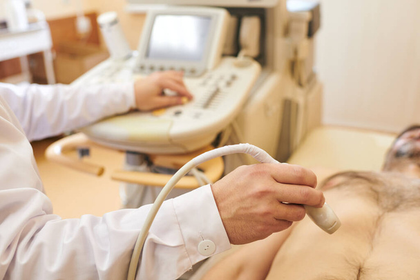 Ultraääniluotaimella toimivan tunnistamattoman ultraäänitutkijan lähikuva potilaan vatsan tarkistamisen yhteydessä
 - Valokuva, kuva