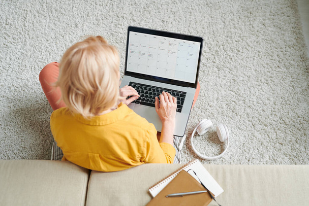 Mujer rubia en ropa de casualwear sentado en el suelo delante de la computadora portátil y mirando a través de los datos en pantalla mientras trabaja en el entorno doméstico
 - Foto, imagen
