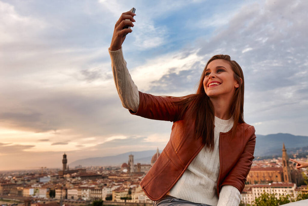 Una joven tomando una foto de sí misma con un panorama de Florencia detrás de ella
. - Foto, Imagen