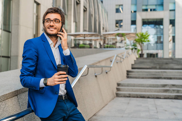 Smiling business man with cup of coffee talking on cell phone in downtown - 写真・画像