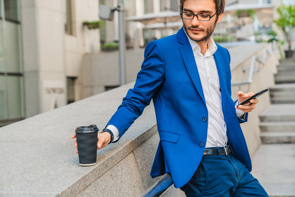 Young caucasian man in formalwear taking coffee cup while having break at city street - Fotoğraf, Görsel