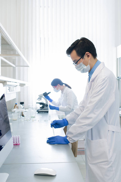 Jovem farmacêutico ou pesquisador chinês testando nova vacina enquanto seu colega estuda as características do vírus em segundo plano
 - Foto, Imagem