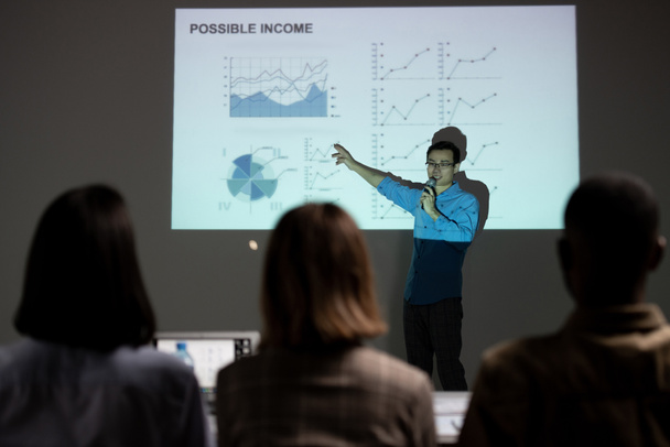 Zelfverzekerde Aziatische financiële specialist schilderen op projectiescherm, terwijl het voorspellen van de inkomsten op zakelijke bijeenkomst - Foto, afbeelding