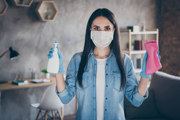 Photo of housemaid lady stay home quarantine use anti virus mask applying spray antiseptic cleaning soap hold rag cleaning house hands wear gloves facial protective mask living room indoors - Foto, Imagen
