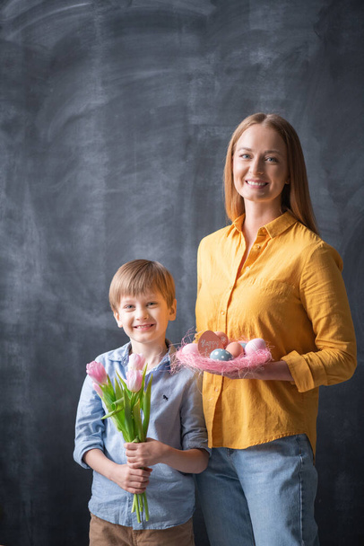 Portrait of cheerful family with Easter nest and bunch of tulips posing against blackboard - Photo, Image