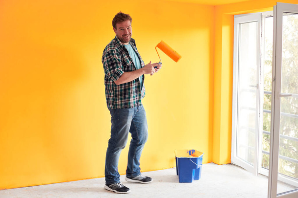 Jeune homme peignant un mur sur la couleur du tournesol dans une maison moderne
 - Photo, image