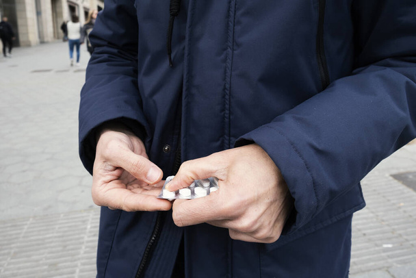 zbliżenie białego mężczyzny na ulicy, ubranego w niebieską kurtkę, biorącego pigułkę z blistra - Zdjęcie, obraz