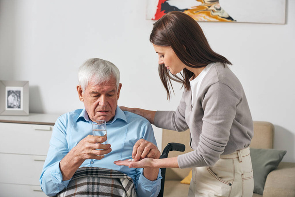 Fiatal felnőtt lánya gyógyszert ad az idősebb apának, miközben a stroke után gondozza. - Fotó, kép