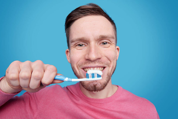 Ευτυχισμένος νεαρός άνδρας με υγιές χαμόγελο πρόκειται να βουρτσίσει τα δόντια του, ενώ κρατώντας οδοντόβουρτσα από το στόμα στην απομόνωση - Φωτογραφία, εικόνα