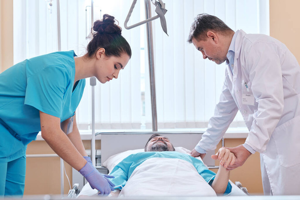 Pielęgniarka i lekarz stojący przy łóżku szpitalnym i sprawdzający stan pacjentów - Zdjęcie, obraz