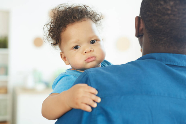 Portrait of cute African-American baby looking at camera while sitting in fathers arms, copy space - Photo, Image