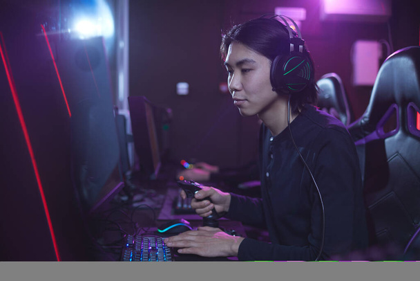 Portrét mladého Asiata hrající videohry pomocí závodní posun v temném kybernetickém interiéru, kopírovací prostor - Fotografie, Obrázek