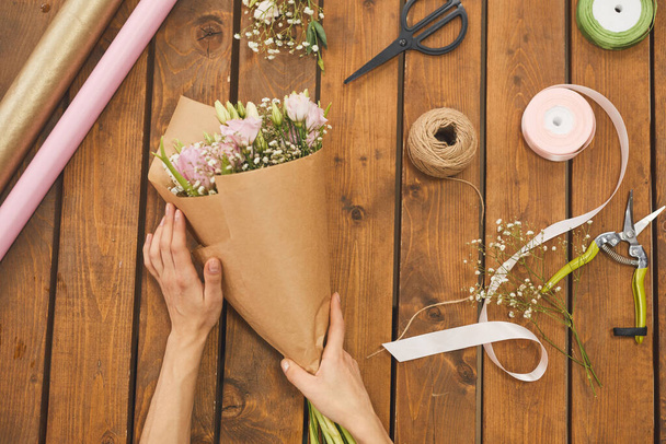 Above view background of female hands decorating flower bouquet on wooden table with craft supplies, copy space - Fotografie, Obrázek