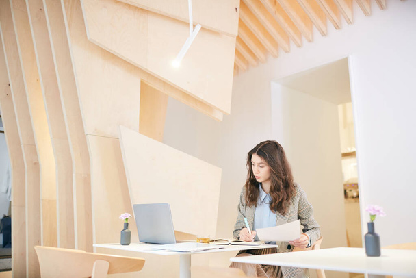 Retrato de gran angular de una mujer joven y bonita que trabaja en el escritorio en el interior de diseño arquitectónico, espacio de copia - Foto, imagen