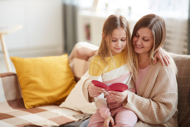 Warm-toned portrait of happy mother hugging daughter while reading holiday card on Mothers day, copy space - Foto, Imagem
