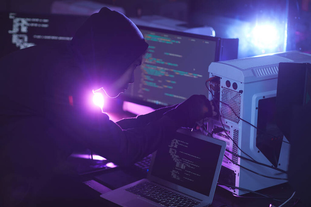 Sivunäkymä tunnistamaton cyber turvallisuus hakkeri yllään huppu työskennellessään tietokonejärjestelmän pimeässä huoneessa, kopioi tilaa
 - Valokuva, kuva