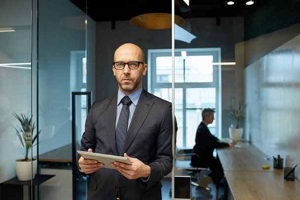 Талия портрет успешного лысого бизнесмена, стоящего в современном офисе интерьера холдинга планшет, копировать пространство
 - Фото, изображение