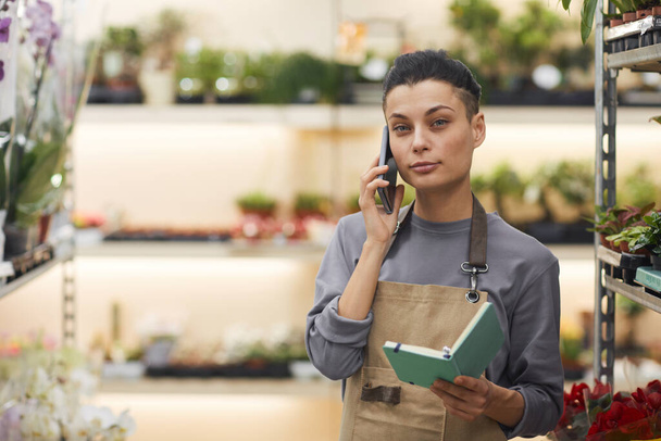 Waist up portrait of successful female business owner speaking by smartphone while standing in flower shop, copy space - Photo, Image