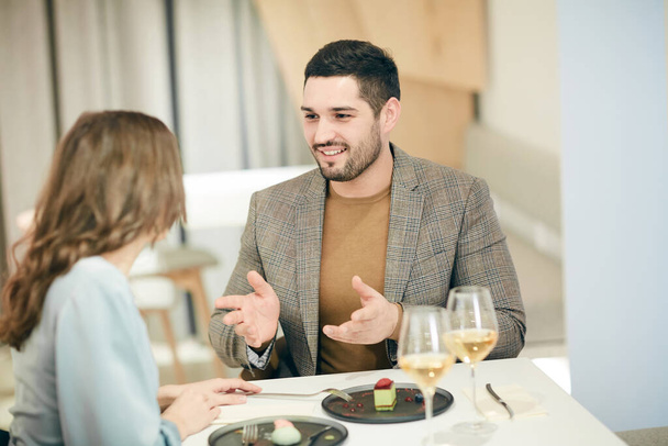Retrato de ángulo alto mínimo de pareja moderna hablando y haciendo gestos mientras disfruta de una cita romántica en la cafetería, espacio para copiar - Foto, Imagen