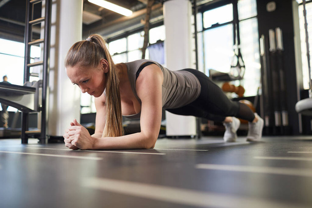 Полнометражный портрет спортивной молодой женщины, делающей упражнения на доске во время силовых тренировок в современном тренажерном зале, копировальное пространство
 - Фото, изображение
