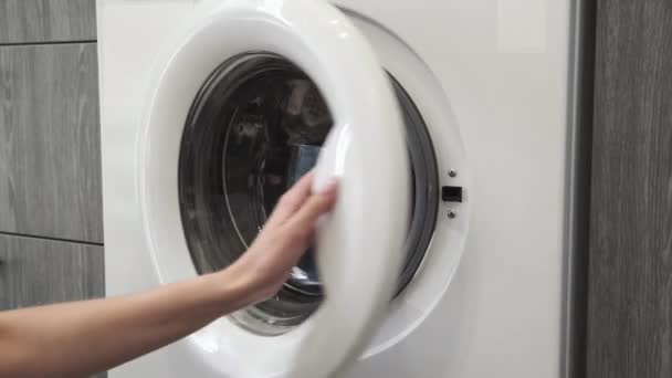 Γυναικείο χέρι παίρνει JEANS από πλυντήριο. Φόρτωση πλυντηρίου. Φόρτωσε ρούχα στο πλυντήριο. Φορτώστε ρούχα πλυντήριο ρούχων. Προετοιμασία πλυσίματος ρούχων - Πλάνα, βίντεο