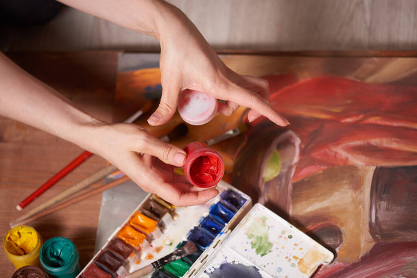 Мастер на работе рисует гуашь красками, натюрморт. Краска банки и кисти руки мастера
. - Фото, изображение