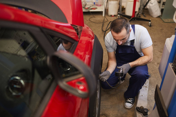 Vue grand angle au mécanicien de voiture vérifiant la pression dans les pneus lors de l'inspection du véhicule dans l'atelier de garage, espace de copie
 - Photo, image