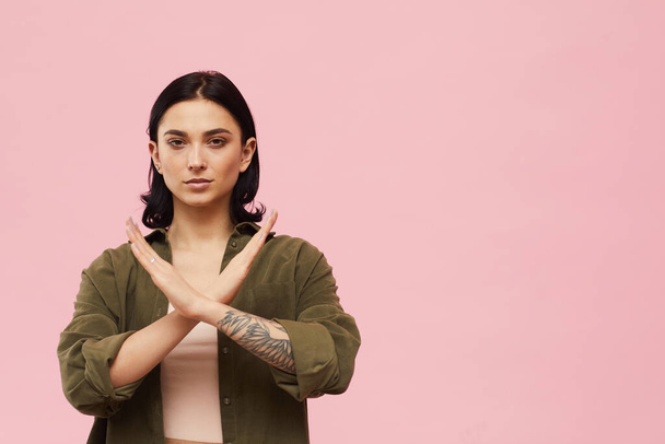 Derék fel portré a modern fiatal nő mutató NO gesztus és a kamerába, miközben áll szemben rózsaszín háttér stúdió, másolás tér - Fotó, kép