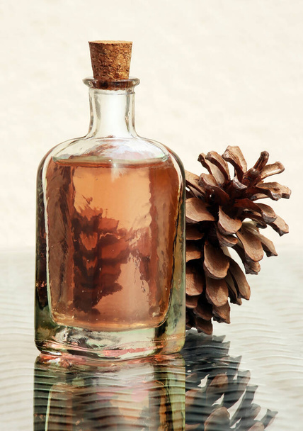 Still life with essential aroma oil in vintage glass bottle and pine cone against a high key background. Amazing reflections, selective and soft focus.  - Foto, afbeelding