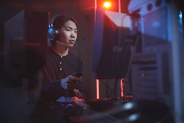 Siyah siber ortamda yarış kayması kullanarak video oyunu oynayan Asyalı genç adamın portresi, kopyalama alanı - Fotoğraf, Görsel