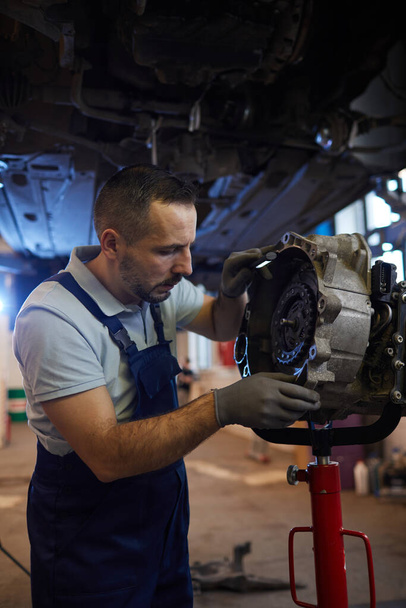 Vertical portrait of bearded car mechanic repairing gearbox in auto workshop, copy space - Fotoğraf, Görsel