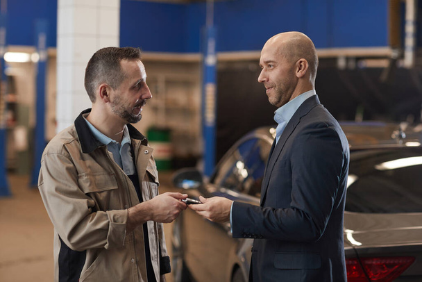 Waist up portrait of mechanic giving keys to mature businessman after checking luxury car at annual inspection, copy space - Photo, Image