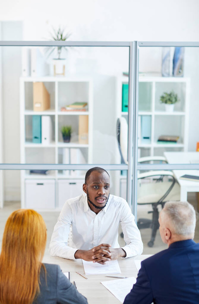 Magas látószögű nézet a kortárs afro-amerikai férfi válaszol kérdésekre HR menedzser állásinterjú során az irodában, másolás tér - Fotó, kép