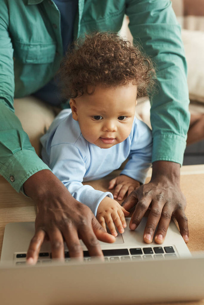 ラップトップを使用してかわいいアフリカ系アメリカ人の赤ちゃんの垂直肖像画と父親と画面を見て、スペースをコピー - 写真・画像