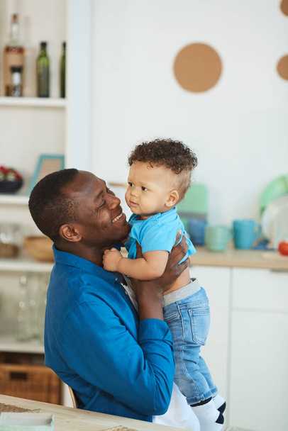 Porträt eines glücklichen afroamerikanischen Vaters, der mit einem kleinen Jungen weiß spielt, der am Küchentisch sitzt, Kopierraum - Foto, Bild