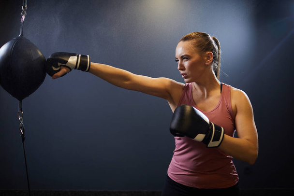 Side view portrait of determined young woman boxing with punching bag during fight training or workout, copy space - Photo, Image