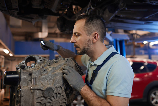 Portrait latéral du mécanicien automobile inspectant la boîte de vitesses dans l'atelier de réparation automobile, espace de copie
 - Photo, image