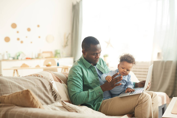 retrato de maduro afro-americano homem usando laptop enquanto babá bonito pequeno filho em casa, cópia espaço
 - Foto, Imagem