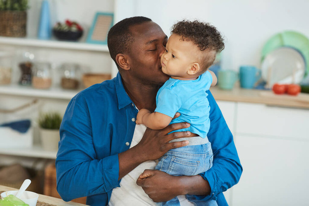 Retrato de papá afroamericano feliz besando lindo niño blanco sentado en la mesa de la cocina, espacio de copia
 - Foto, imagen