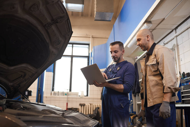 Portrait latéral de deux mécaniciens automobiles utilisant un ordinateur portable lors de l'inspection du véhicule dans un atelier de réparation automobile, espace de copie
 - Photo, image