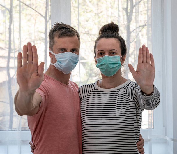 Концепция здравоохранения. Грустная пара в масках позирует у окна дома
 - Фото, изображение